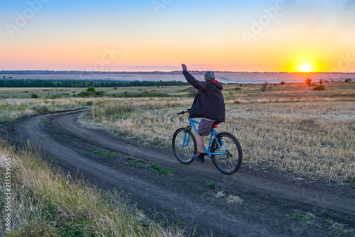 man ride a bike in the country on the field in the evening