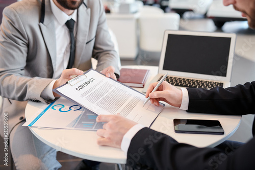 Close-up of businessman sitting at the table and signing a contract giving his colleague