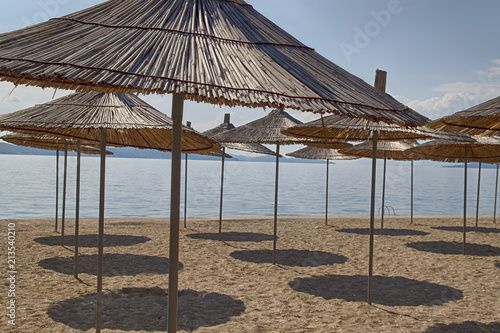 a lot of straw beach umbrellas on the beach, casting a shadow