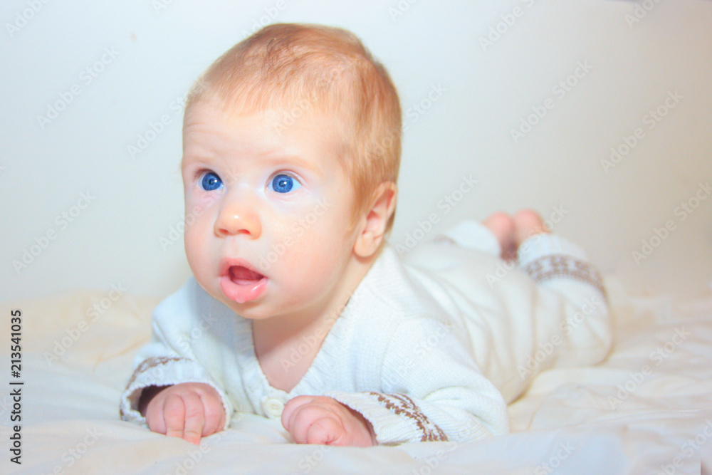 A baby with blue eyes looks up. A sweet baby lies on his stomach and learns to hold his head.