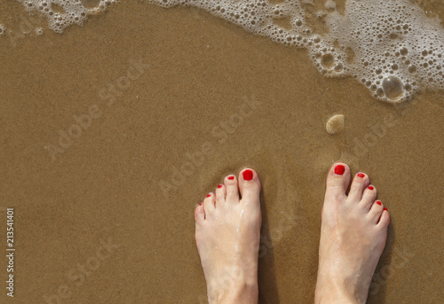 Women bare feet with red nails on sea beach, wave with sea foam. Summer, heat, sunny day travel, freedom, enjoy and relaxation