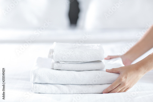 Close-up of hands putting stack of fresh white bath towels on the bed sheet. Room service maid cleaning hotel room.
