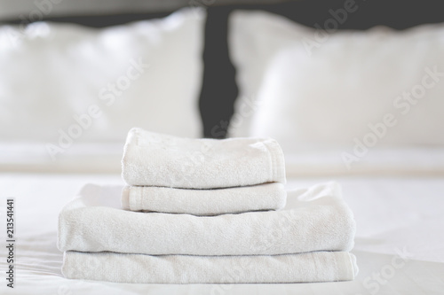Close-up of hands putting stack of fresh white bath towels on the bed sheet. Room service maid cleaning hotel room.