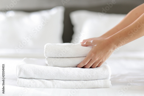 Close-up of hands putting stack of fresh white bath towels on the bed sheet. Room service maid cleaning hotel room.