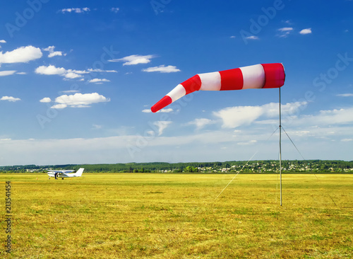 red and white windsock wind sock on blue sky on the aerodrome, yellow field and clouds background photo