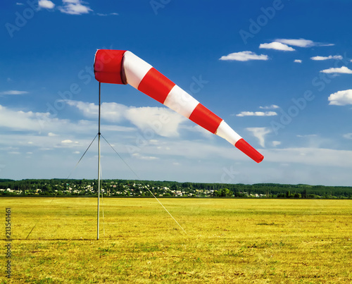 red and white windsock wind sock on blue sky on the aerodrome, yellow field and clouds background