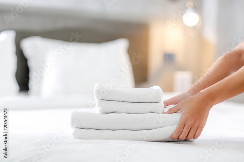Fotografiet Close-up of hands putting stack of fresh white bath towels on the bed sheet