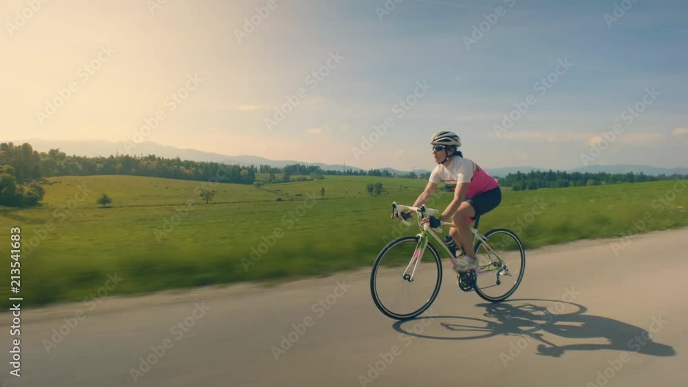 wide tracking shot of a single female cyclist on the countryside road