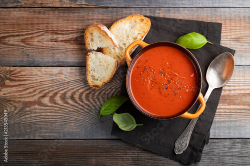 Homemade tomato soup with Basil, toast and olive oil on a wooden table. Prepared a vegetarian dish on a dark background. Top view with copy space