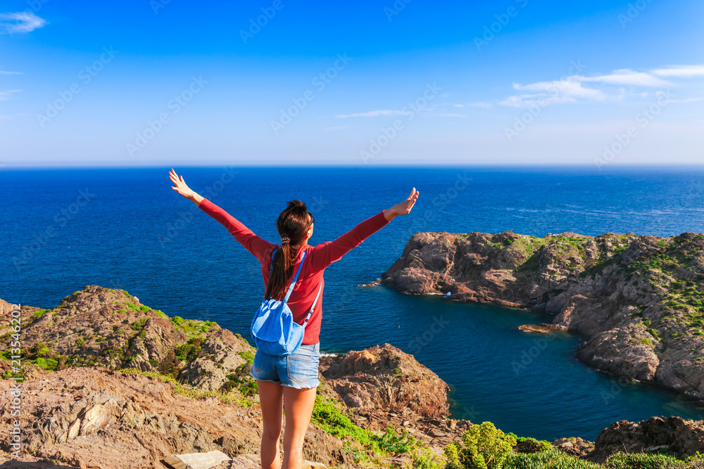 Tourist woman with backpack on Cap de Creus, natural park. Eastern point of Spain, Girona province, Catalonia. Famous tourist destination in Costa Brava. Sunny summer day with blue sky and clouds