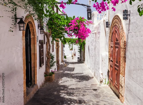 Obraz Wąska ulica w Lindos miasteczku na Rhodes wyspie, Dodekanez, Grecja. Piękni sceniczni starzy antyczni biel domy z kwiatami. Znane miejsce turystyczne w Europie Południowej