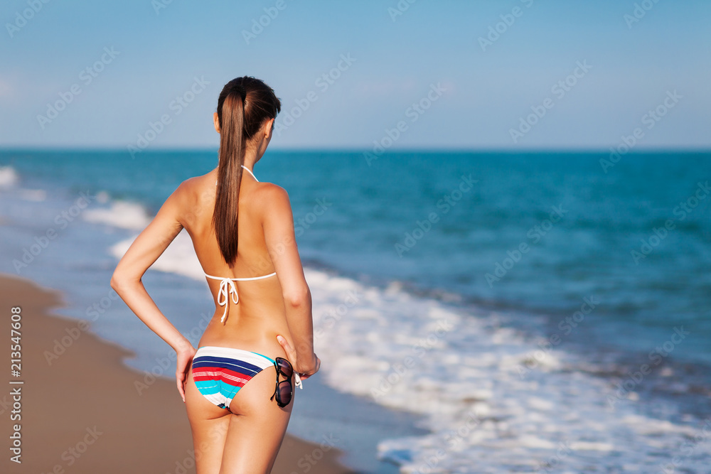 Sexy back of a beautiful woman in bikini on sea background. Sexy buttocks. Soft sunset light.