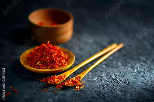 Saffron spices. Saffron on black stone table in a wood bowl and a spoon. Spice and herbs on slate background. Cooking ingredients photo