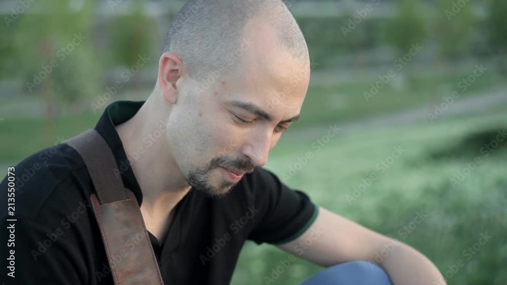 A young man sitting in the Park with a phone and writing a text message A young man sitting in the Park with a phone and writing a text message