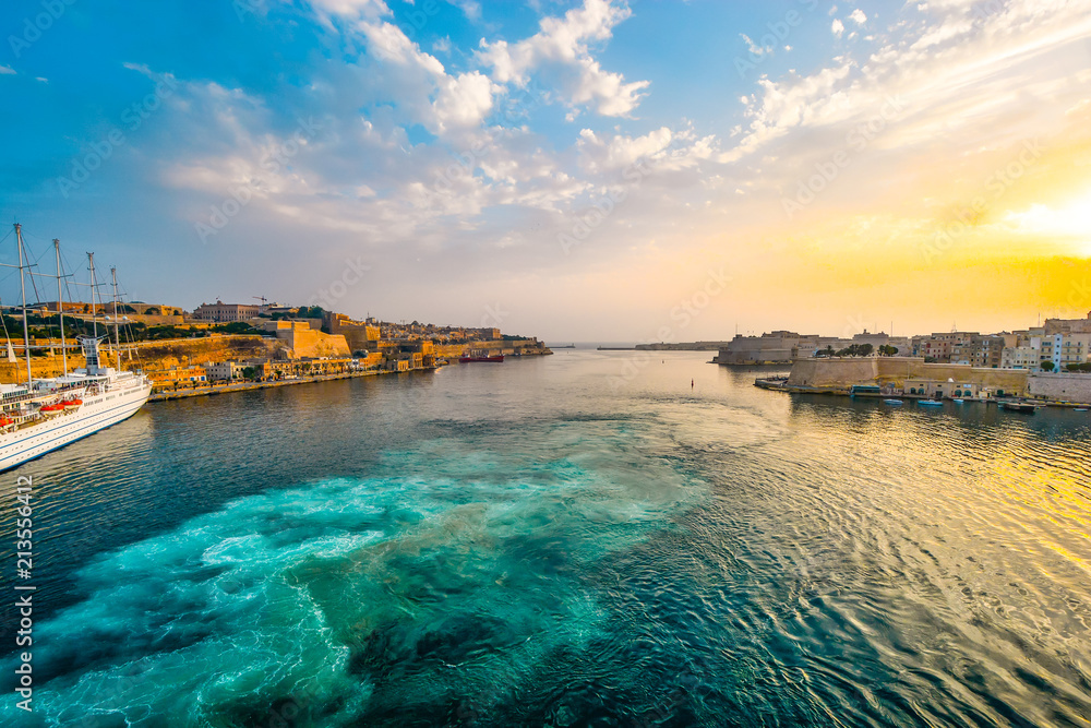 Sunrise at the Grand Harbour of Valletta Malta with sun hitting the old city and a small cruise ship