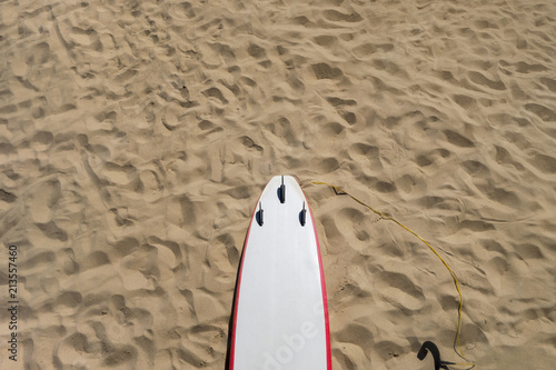 sand with footsteps back top of a white red surfboard