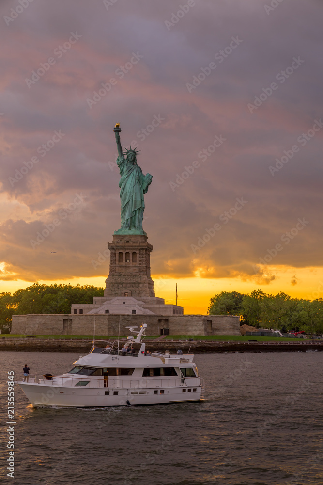 Sunset view of Statue of Liberty with sailboat passing by in New York Harbor