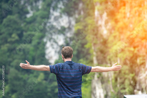 young man happy with hands rise up on beautiful lake and mountain Landscape with beautiful cloudy sky.