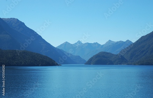 A study in blue - a clear blue sky  light blue water of a lake and jagged blue mountains. Snow is on the distant mountain tops.