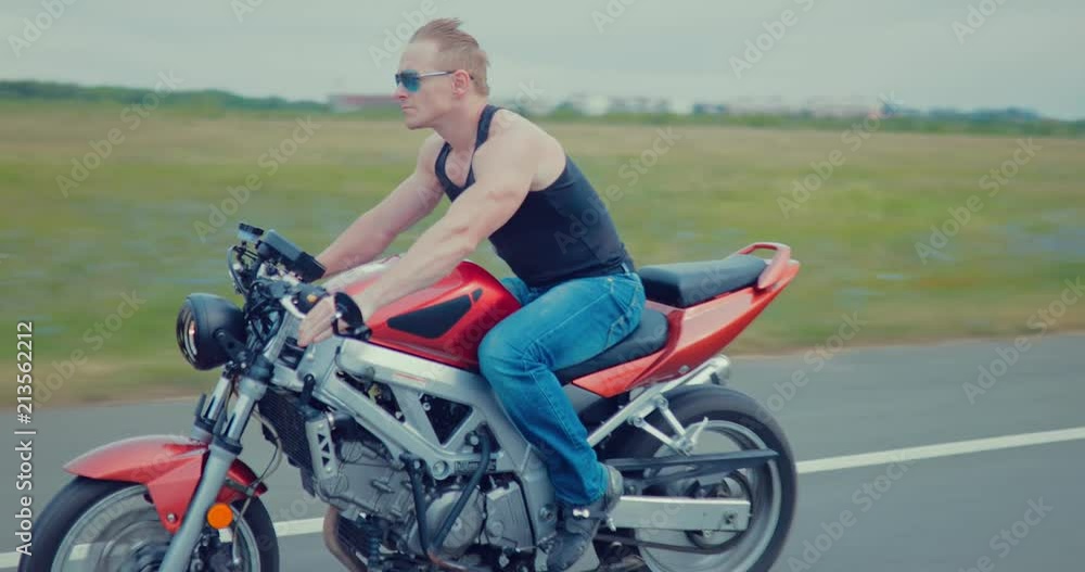 Stylish cool young man in sunglasses riding motorcycle on a asphalt road Stylish cool young man in sunglasses riding motorcycle on a asphalt road