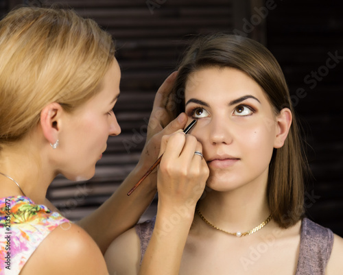 Eye makeup woman applying eyeshadow powder. Stylist is doing make up for female by eyeliner
