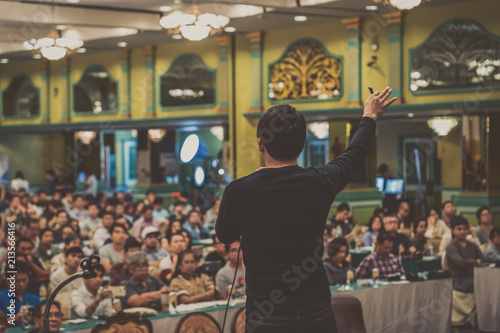 Rear view of Asian Speaker with casual suit standing and giving the knowledge over the photo blurred of audience in the conference hall or seminar meeting, business and education concept