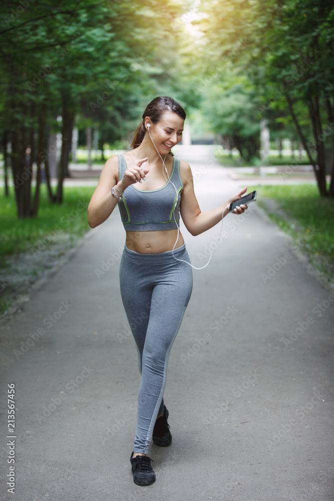 Young woman jogging down a path in a green park.