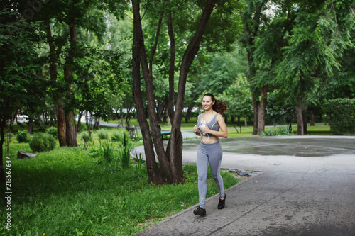 Young woman jogging down a path in a green park.