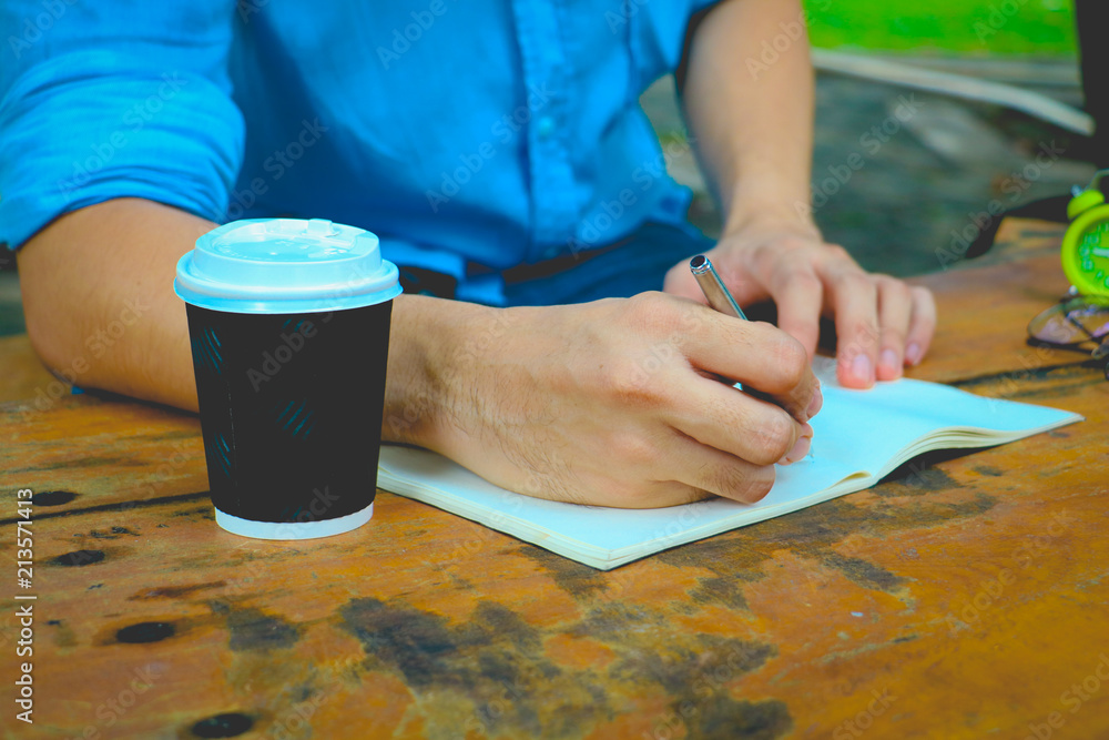 Obraz premium In the morning . Men sitting in the park and he writing notebook. He drinking coffee and working on idea on notebook in relax time .