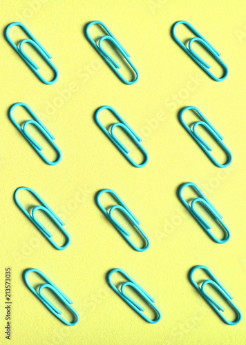 Blue paper clips isolated on yellow background, close up, copy space. Top view, flat lay. Back to school, college, education concept