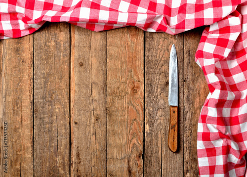 Red checkered tablecloth top and right frame and knife on vintage wooden table background - view from above
