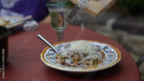 Cinemagraph of a cheese being grated onto an italian bowl of pasta with a glass of white wine in the distance. photo