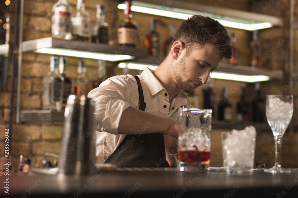 Immersed in work. Handsome young man standing behind a bar counter and working as a barman while creating new drinks