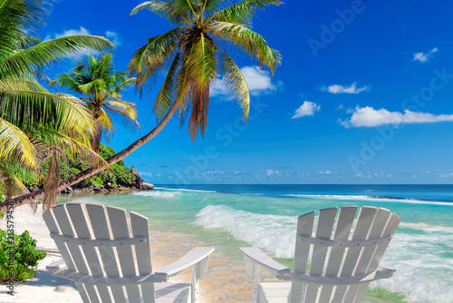 Beach chairs on sandy beach with palm and turquoise sea. Summer vacation and travel concept. 