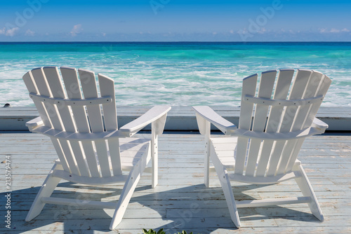 Beach chairs on wooden deck and turquoise sea at sunset. Summer vacation and travel concept.