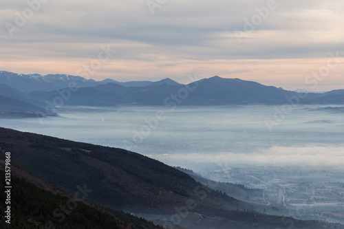 Beautiful aerial view of Umbria valley in a winter morning, with fog covering trees and house and warm colors in the sky