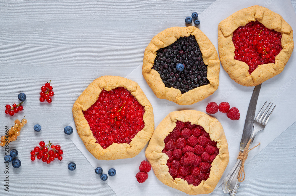 Various berries galette with knife and fork on the gray background. Vegetarian healthy tarts with fresh blueberries, raspberries, red currants. Delicious dessert. Top view with copy space for text Various berries galette with knife and fork on the gray background. Vegetarian healthy tarts with fresh blueberries, raspberries, red currants. Delicious dessert. Top view with copy space for text