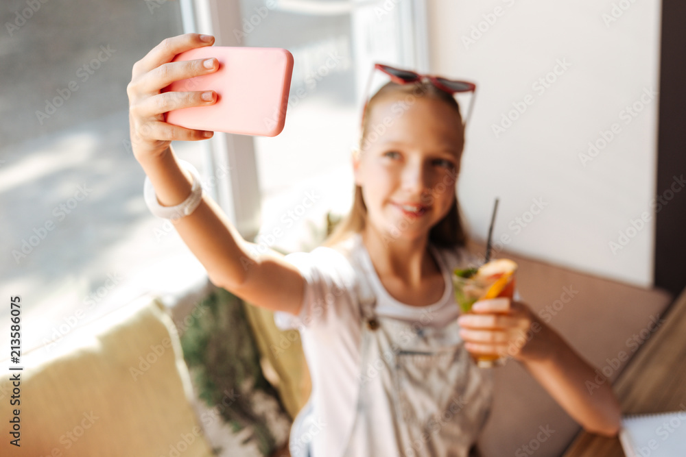 Pink cover. Smiling beaming beautiful teenager holding her phone in pink cover while making selfie Pink cover. Smiling beaming beautiful teenager holding her phone in pink cover while making selfie