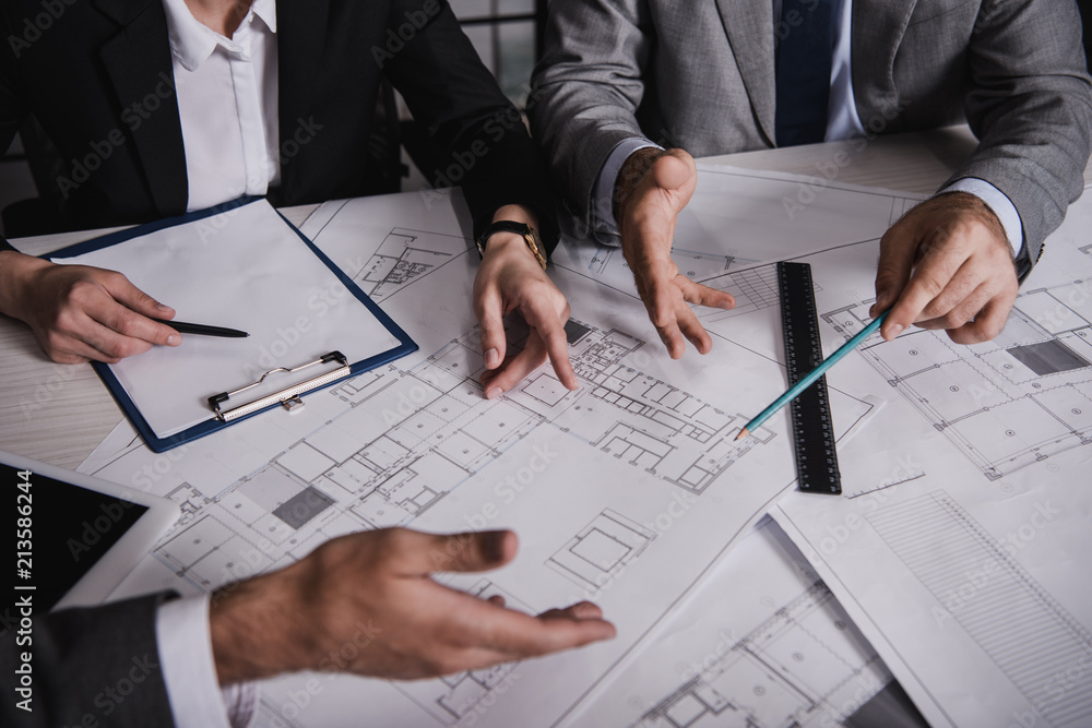 cropped view of architects gesturing and working with blueprints cropped view of architects gesturing and working with blueprints