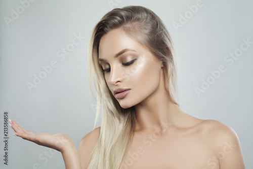 Young Perfect Woman with Natural Makeup, Healthy Skin and Blonde Hair Showing Empty Copy Space on the Open Hand. Facial treatment, Cosmetology, Beauty, Skincare and Spa