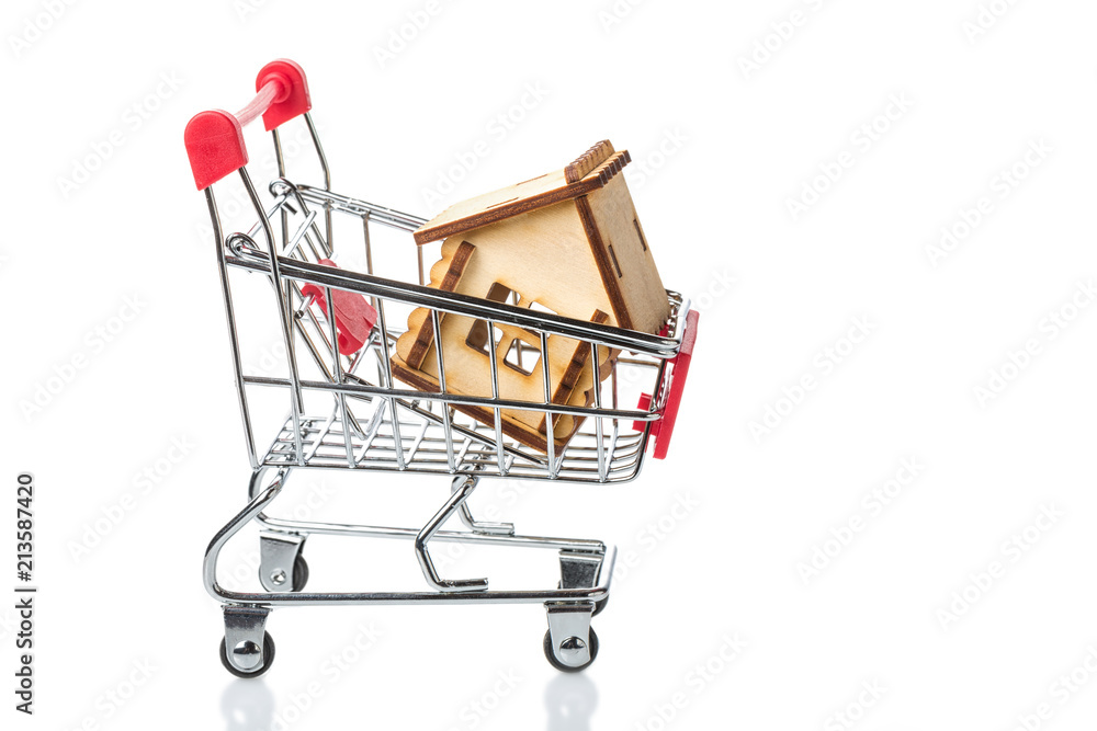 Shopping cart trolley with little wooden house isolated on white. Buying a house or apartment concept.