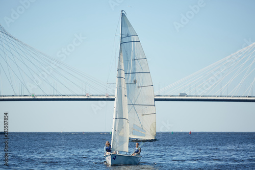 Beautiful sailboat with men on deck floating on river