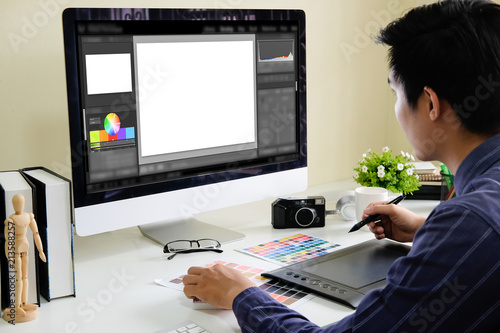 Asian male designer using graphics tablet while working with computer at studio or office.