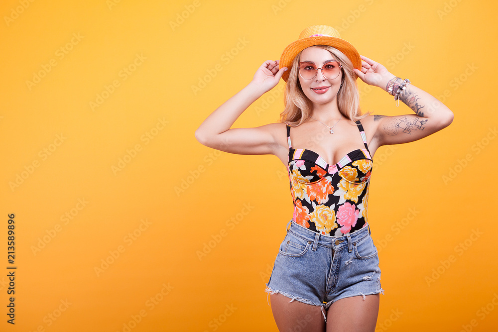 Young sexy slim tanned woman in swimsuit with sunglasses and hat over yellow background Young sexy slim tanned woman in swimsuit with sunglasses and hat over yellow background