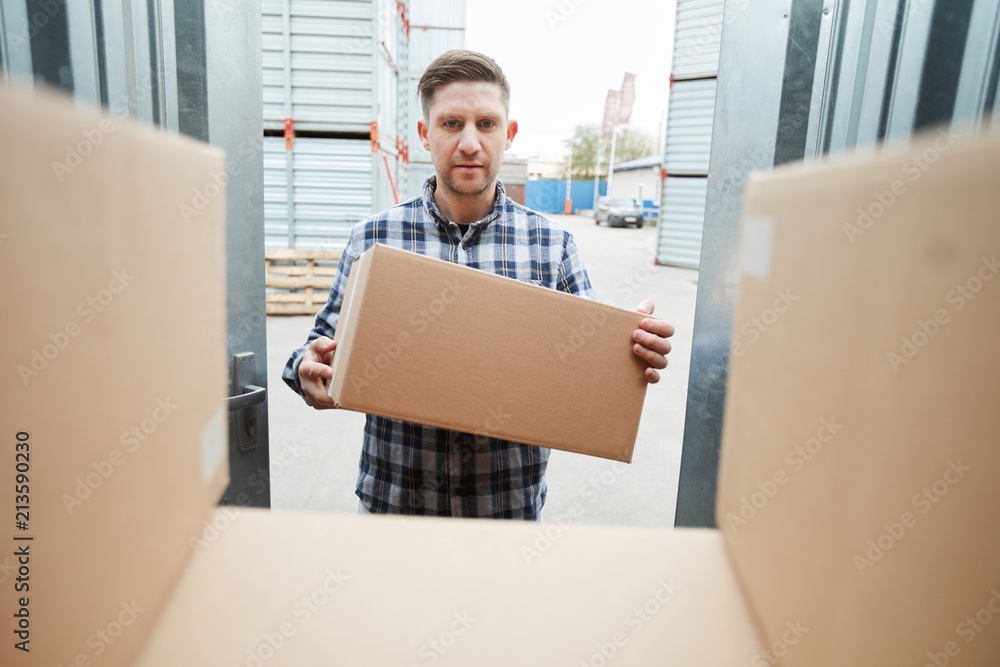 Fotografie Serious handsome man loading container with boxes and putting it on stack of pac
