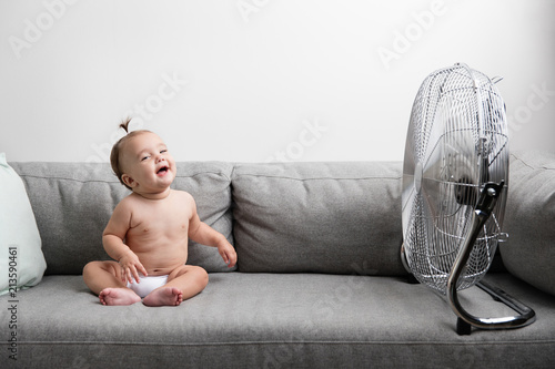 Laughing baby girl sitting on sofa next to fan