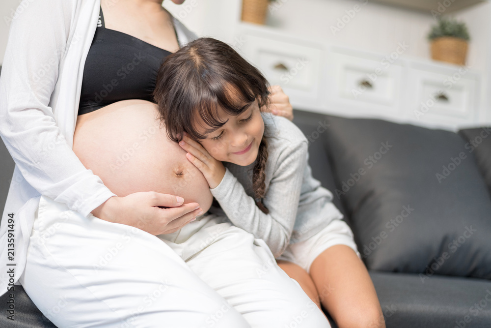 In Selective Focus Of Happy Family Checking New Baby In The Morning.The sister is listening to the baby's voice. Close Up Of A Beautiful Happy Pregnant Woman With Big Belly. In Selective Focus Of Happy Family Checking New Baby In The Morning.The sister is listening to the baby's voice. Close Up Of A Beautiful Happy Pregnant Woman With Big Belly.