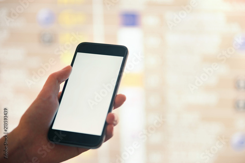 Mockup image of female hands holding black mobile phone with blank white screen over flight board in airport terminal © Bob