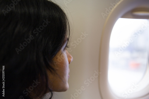 Leaving on a jet plane. Woman Looking through the aircraft window and thinking of home.