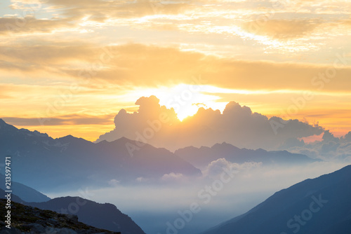 The Alps at sunrise. Colorful sky majestic mountain peaks, fog mist valleys. Sunburst and backlight expansive view from above. © fabio lamanna